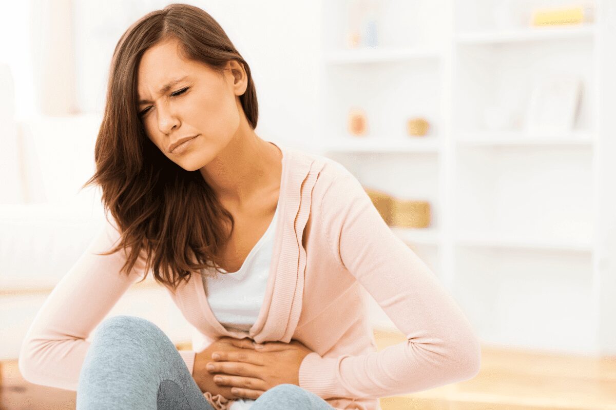 Woman in pink hoodie holding her stomach in discomfort.