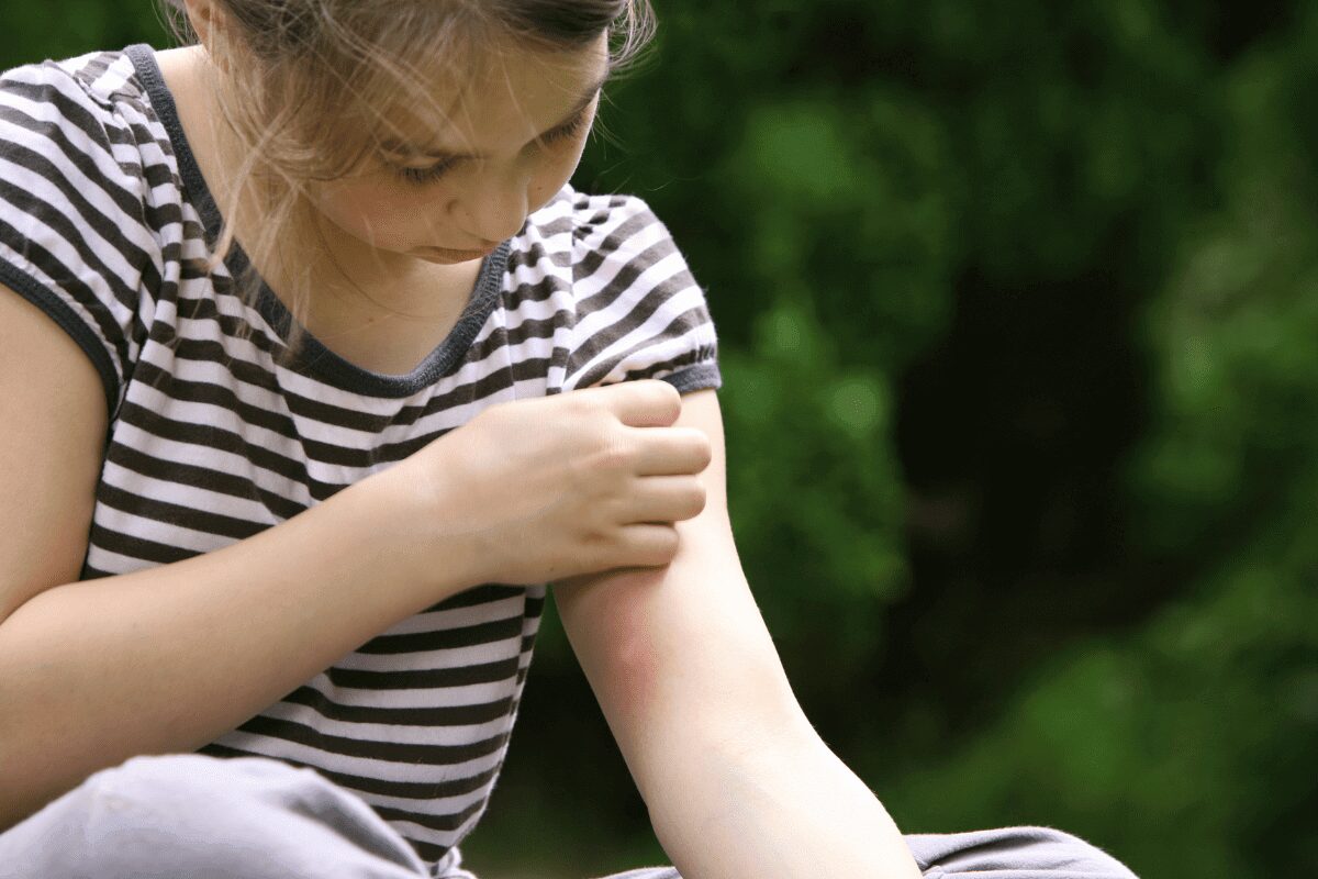 Girl examining a small insect on her arm outdoors.