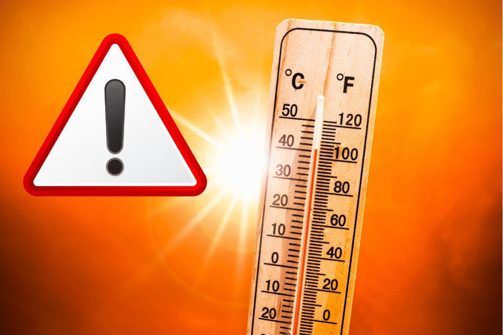 Thermometer showing high temperatures with a warning sign against a bright orange background.