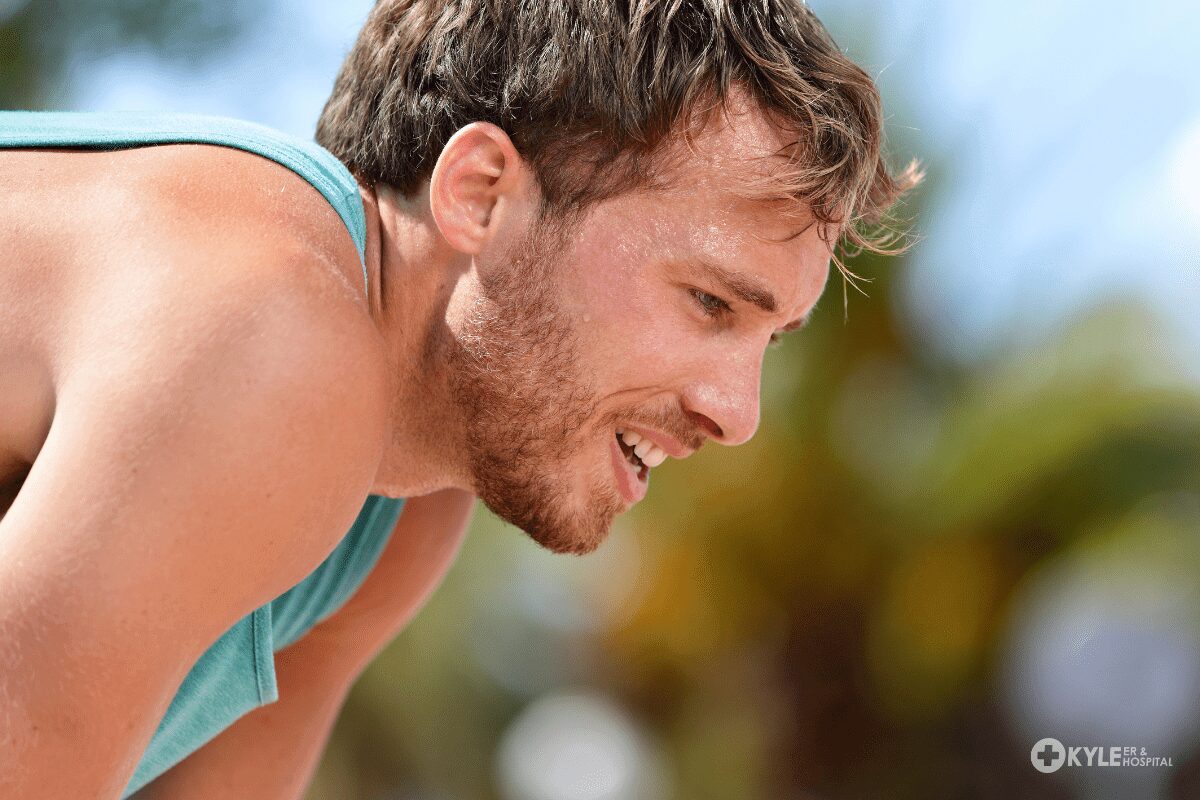 A man smiling warmly outdoors with a blurred natural background.