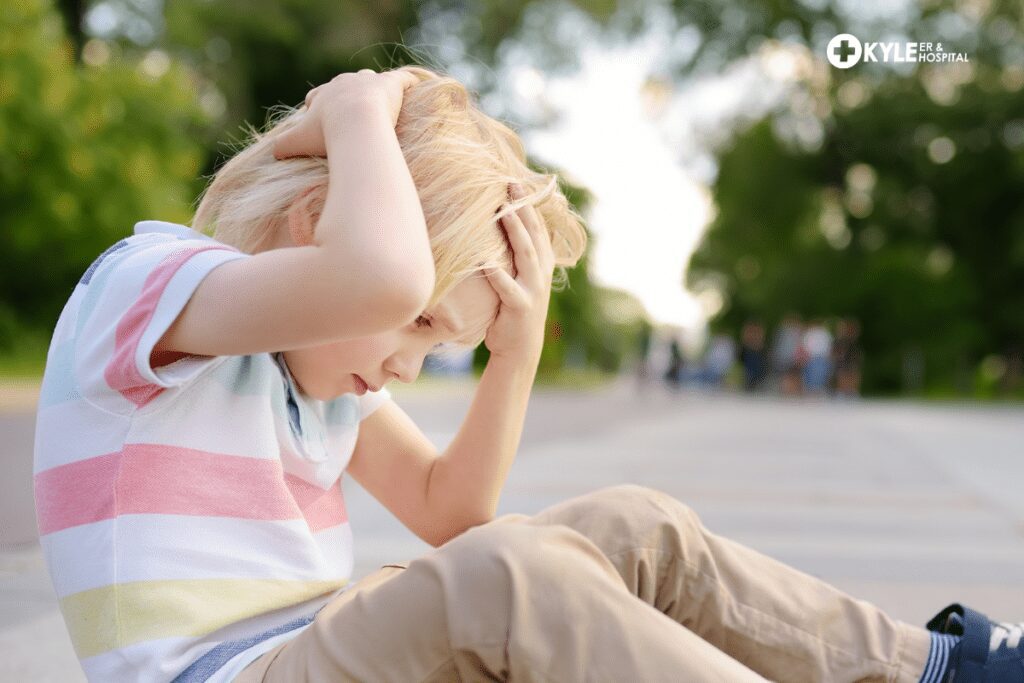 Child sitting with hands on head outside.